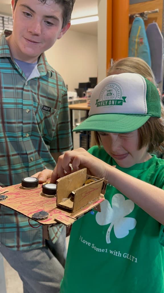 Two campers inspecting a cardboard vehicle with wheels during maker camp