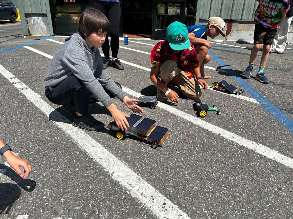 Campers lining up solar-powered cardboard cars for a parking-lot trial